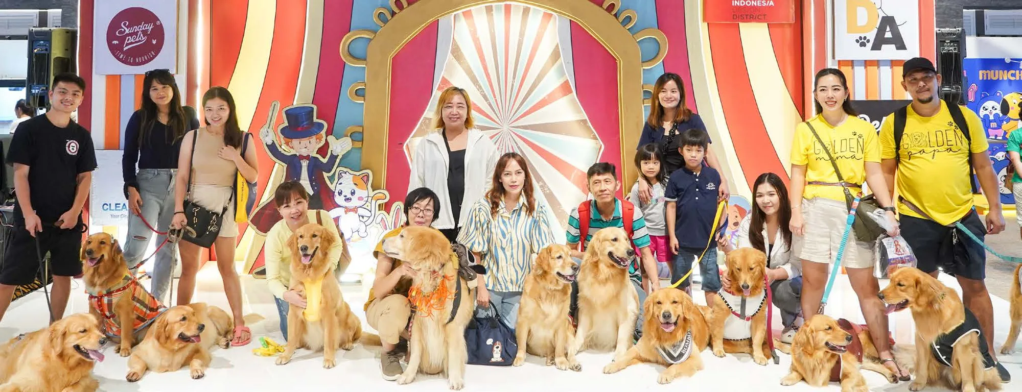 A dozen golden retrievers and their owners posing in front of the main stage at Pet Expo Roadshow
